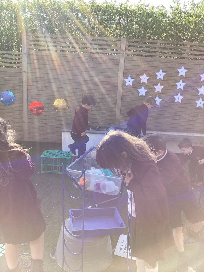 Reception children exploring outdoor learning stations in the sunshine